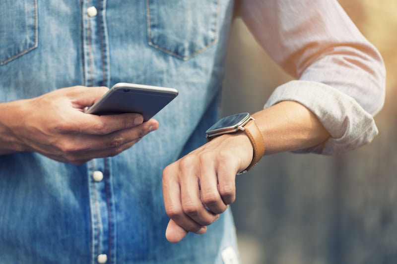 Man looking at smart watch and mobile phone-min