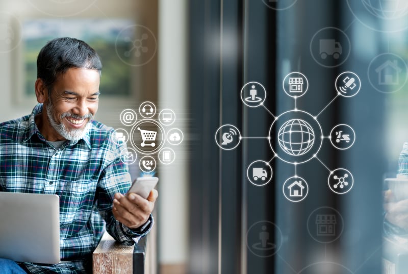 Older man smiling while using laptop and smartphone