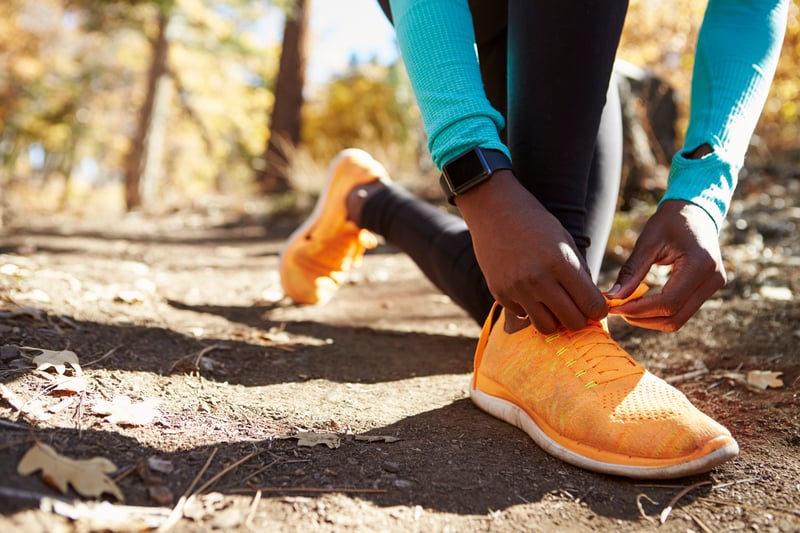 female runner in forest tying shoe