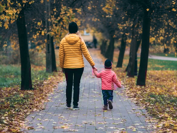 Woman and child walking hand-in-hand in fall