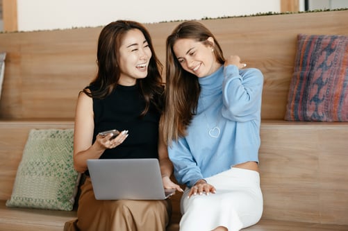 Two young women seated with laptop and smartphone