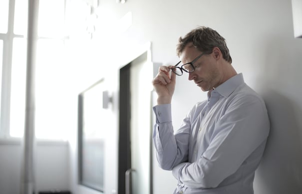 Man with glasses leaning against wall looking stressed