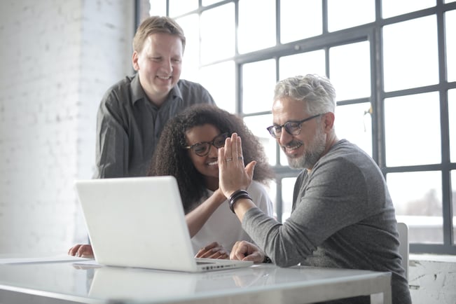 3 employees in front of laptop high-fiving in a modern office space 