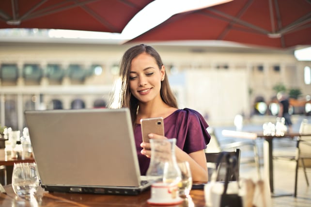 Young woman seated at table with laptop and cellphone