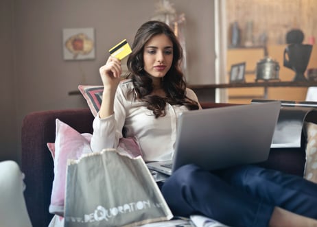 Young woman sitting on couch holding credit card with laptop 