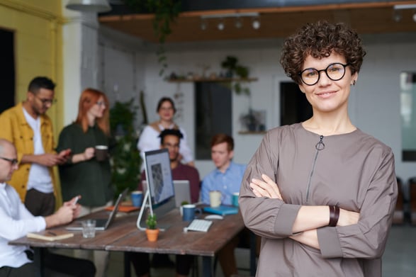 Smiling woman with arms crossed looking at camera with colleagues in background