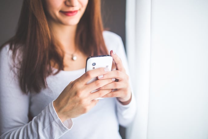 Woman in light grey top looking at cell phone